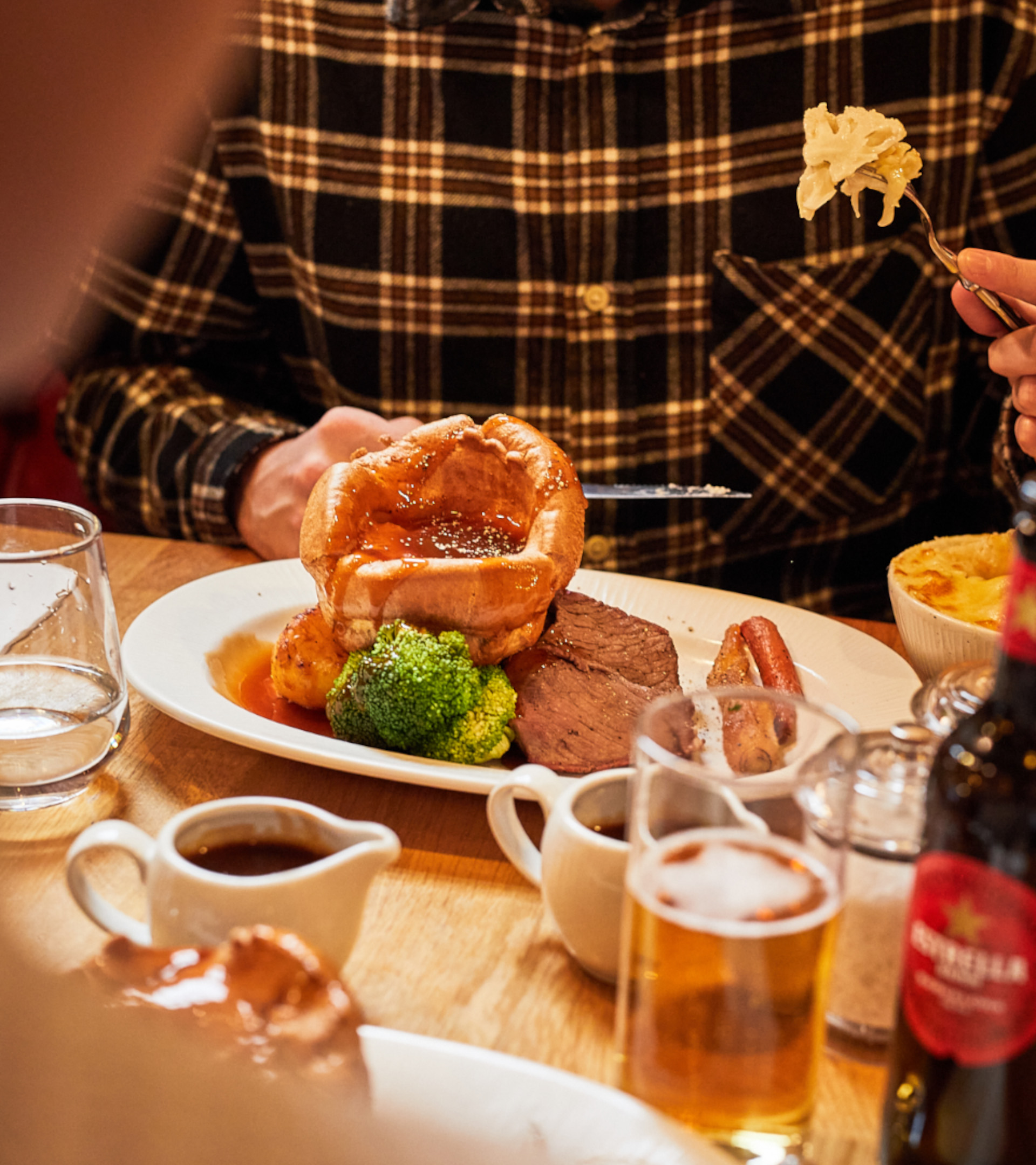 A man eating his main dish with Yorkshire pudding, sauces and Estrella beer.