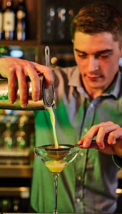 Bartender is pouring cocktail into a martini glass.