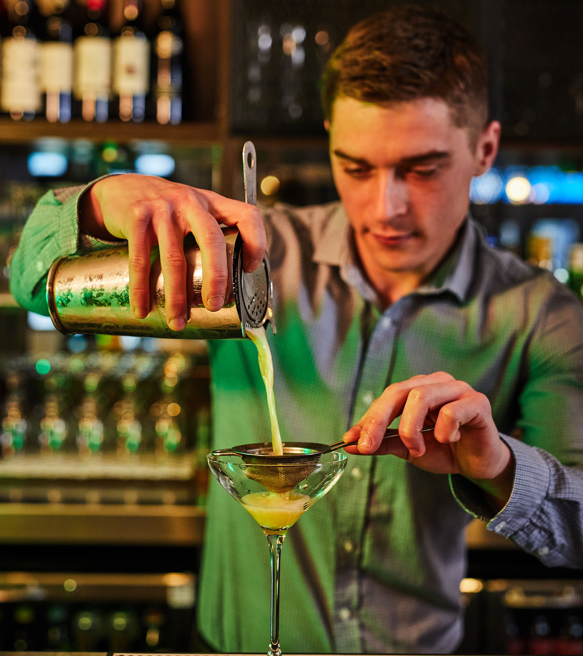 Bartender is pouring cocktail into a martini glass.